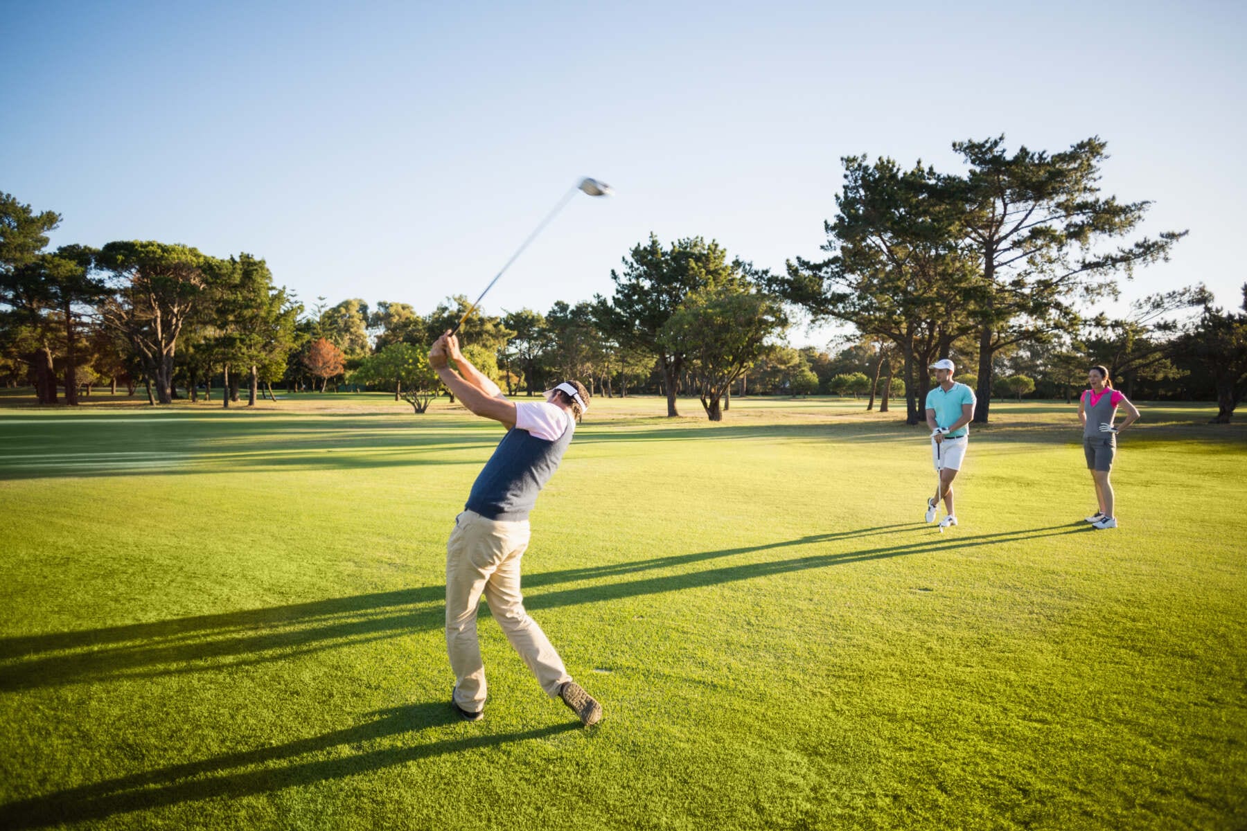 Golfer beim Abschlag auf dem Fairway, zwei Personen beobachten den Schlag bei sonnigem Wetter auf dem Golfplatz. - golf trainer karlsruhe