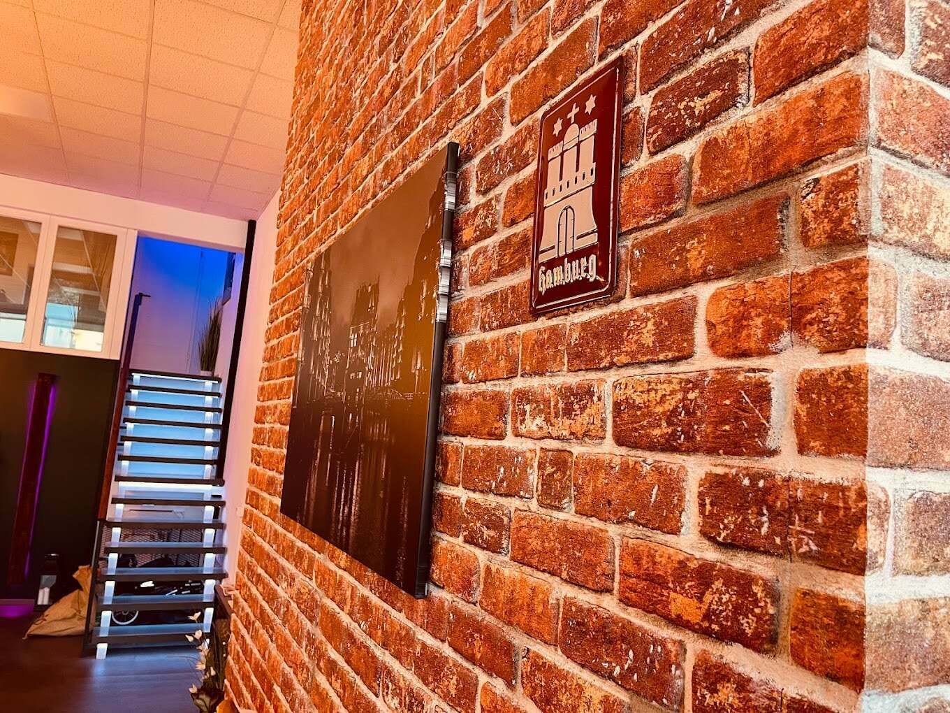 Backsteinwand im Eingangsbereich mit Hamburg-Schild und Treppe, stimmungsvolle Beleuchtung in der Physiotherapiepraxis onebalance Rheinstetten