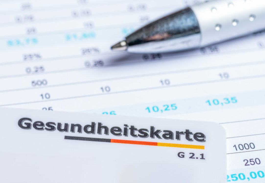 Nahaufnahme einer deutschen Gesundheitskarte auf Formularen mit Zahlen und einem Kugelschreiber, Symbol für Abrechnung und Verwaltung.